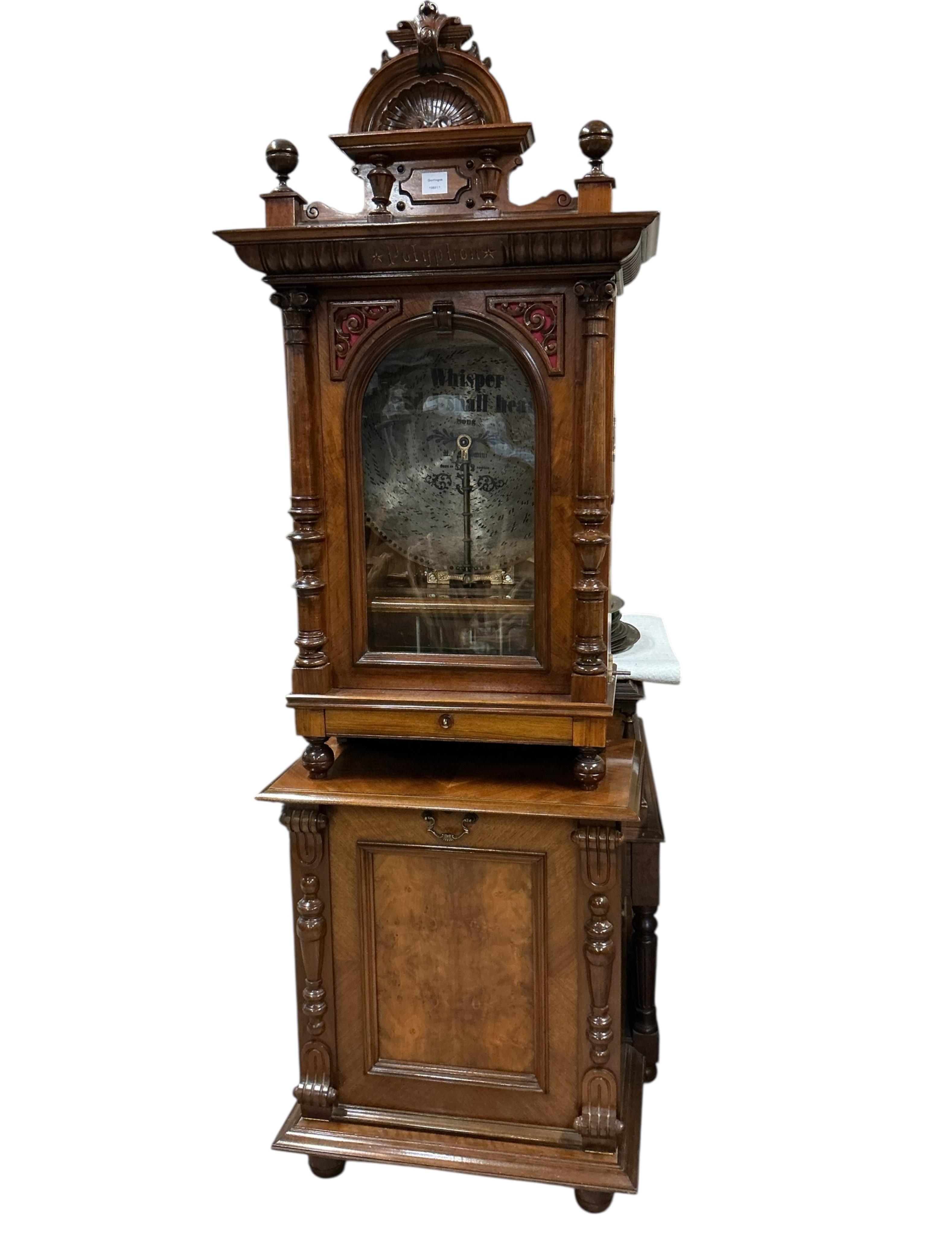 A floor standing coin-operated walnut polyphon disc player with nine 50cm diameter discs, the base containing storage compartments for the discs, coin slots on both sides with guilt finished surrounds next to applied lab